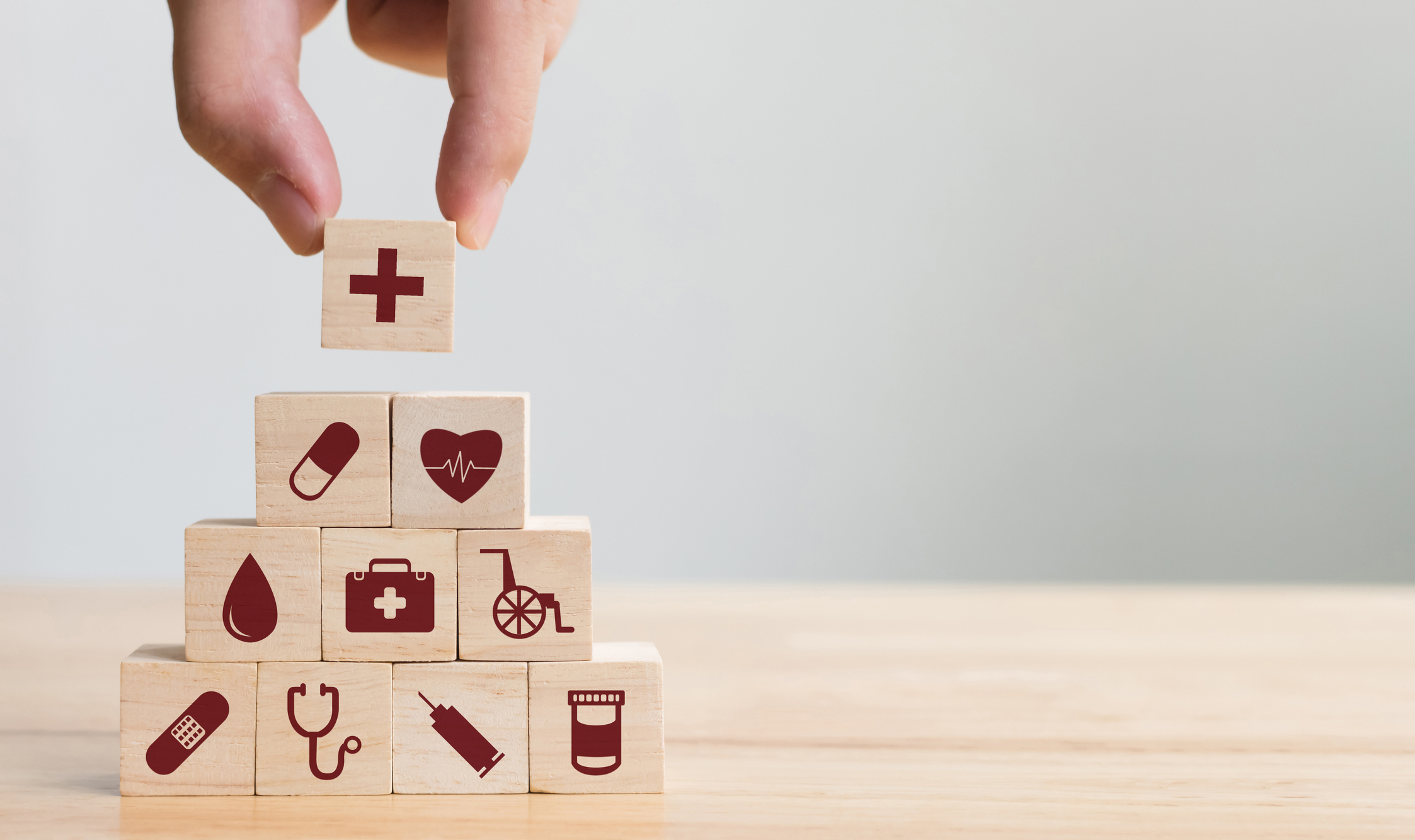 Eine menschliche Hand baut eine Würfelpyramide beschriftet mit Gesundheitssymbolen.